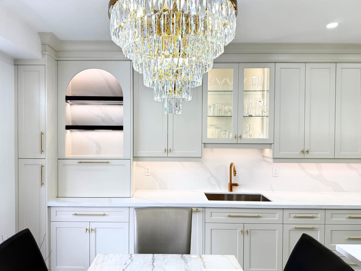 Servery wall with a lit arched display niche, glass-front uppers and a crystal chandelier