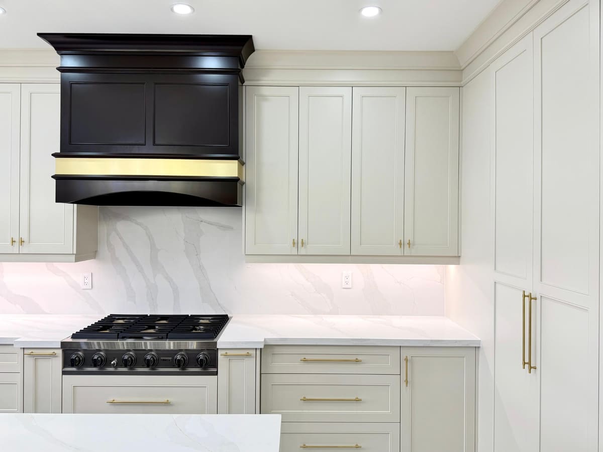 Close-up of a black custom hood with a brass band over a pro range