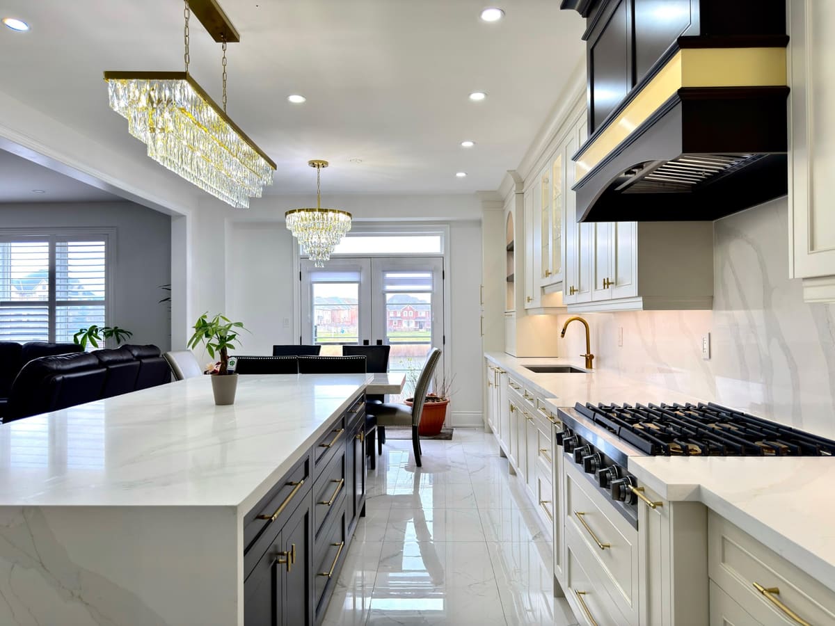 Cream kitchen with a black and brass hood, a waterfall quartz island and crystal chandeliers