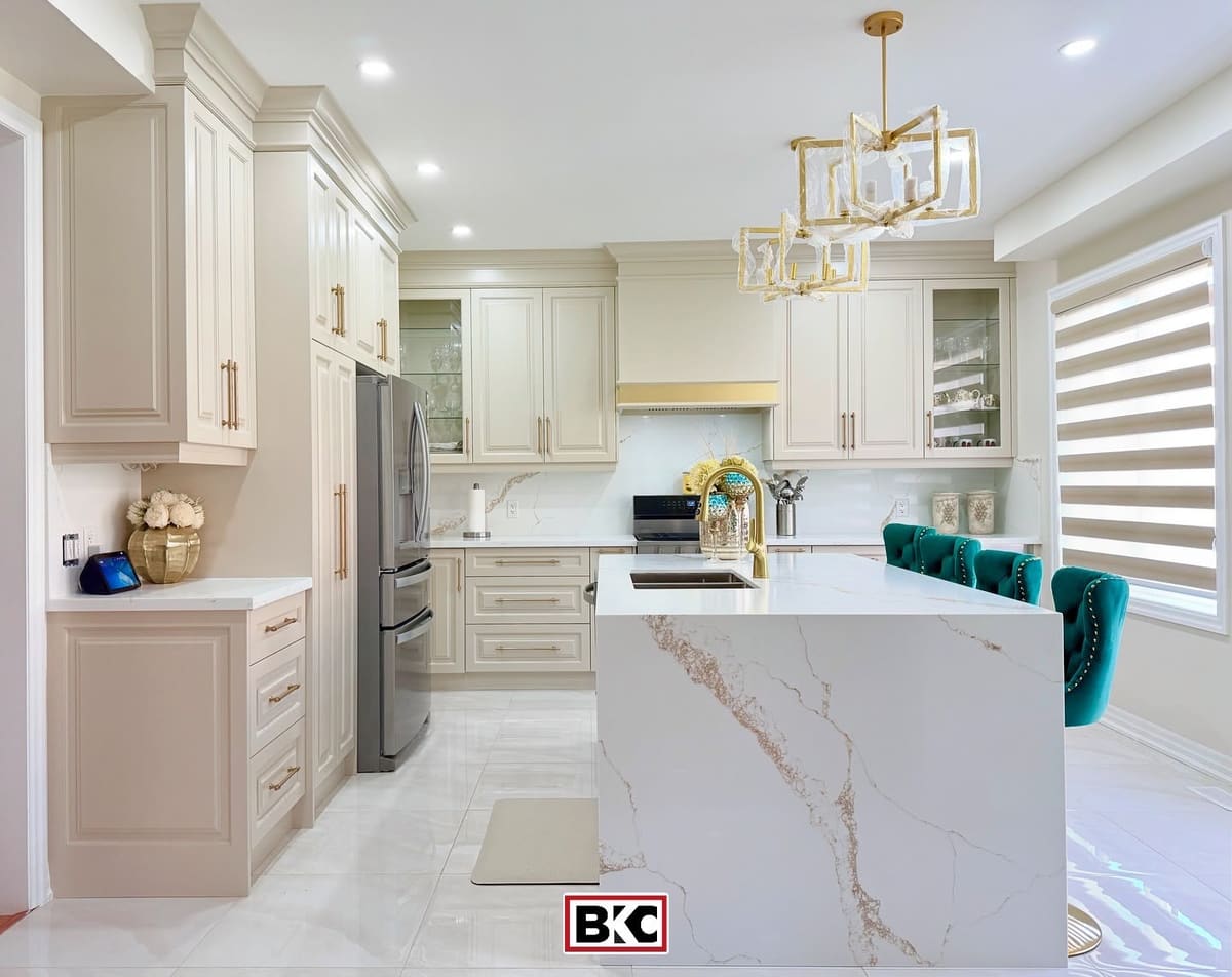 Cream raised-panel kitchen with a gold-veined waterfall island and brass hardware