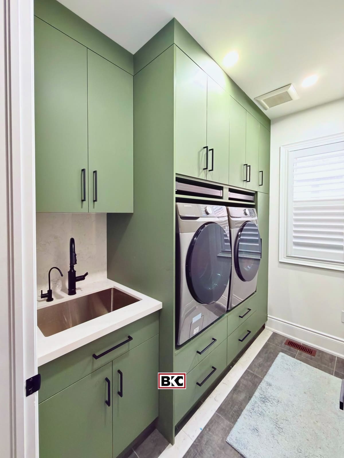 Sage green laundry room with raised washer and dryer, sink and full-height storage
