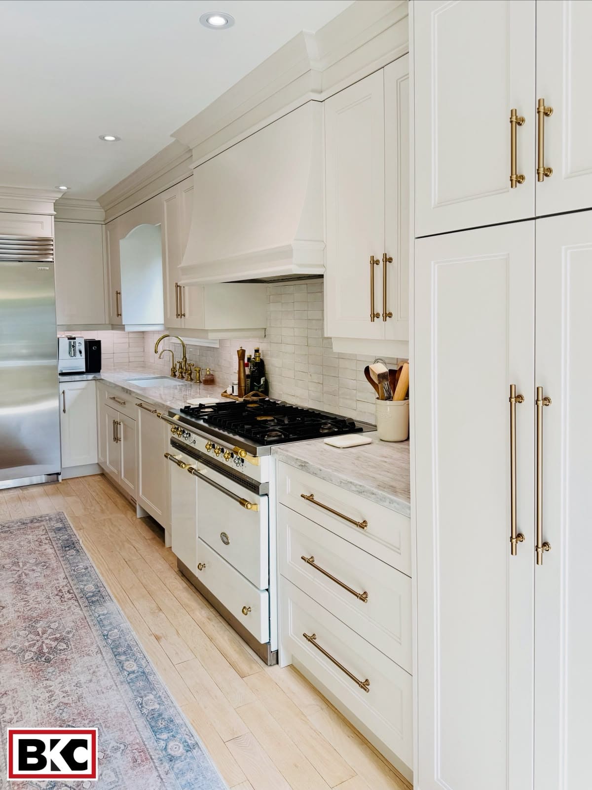 White kitchen with a custom range hood and long brass pulls