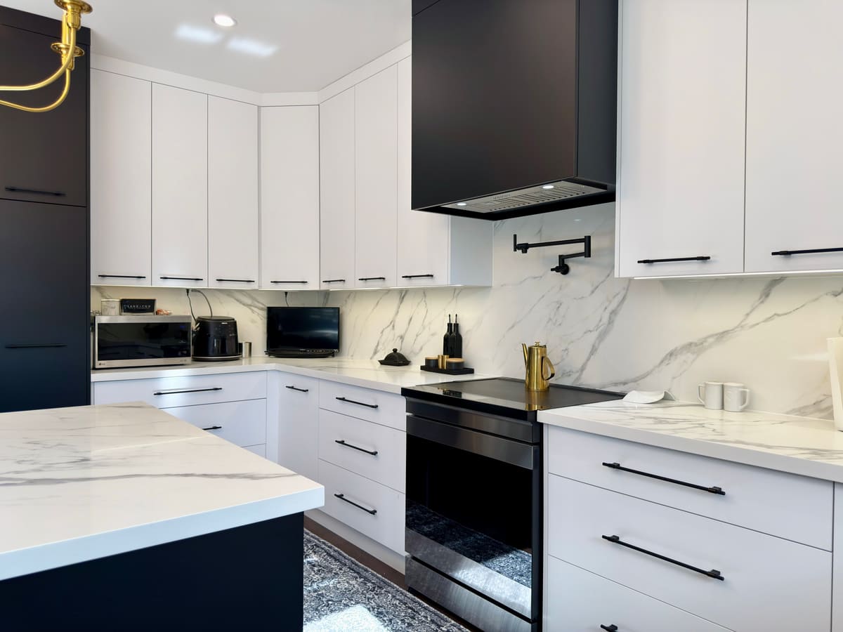White flat-panel kitchen with a black hood and a marble slab backsplash