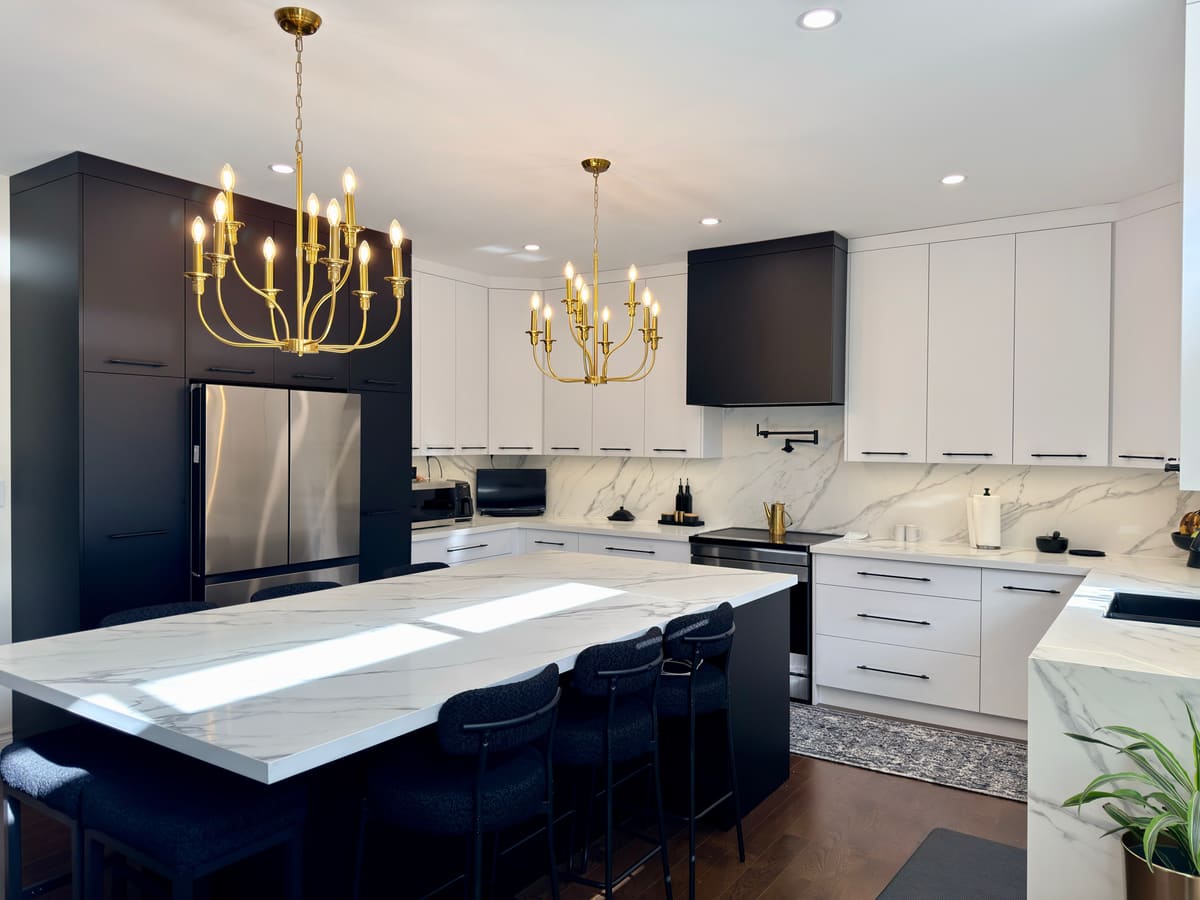 White kitchen with black tall units, a large quartz island and gold chandeliers